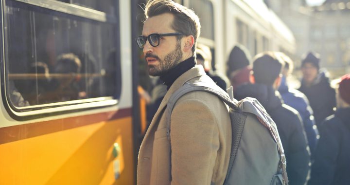 A stylish man with a backpack boards a tram in bustling Budapest, Hungary, during the day.