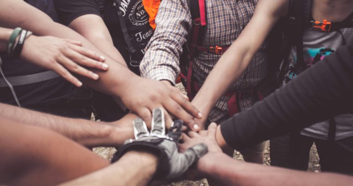 A group of diverse individuals join hands for teamwork in West Java, Indonesia.