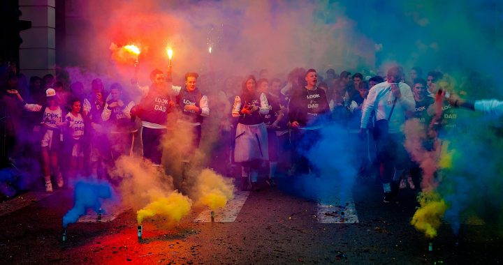 A lively group celebrating at night with color smoke bombs in a street festival.
