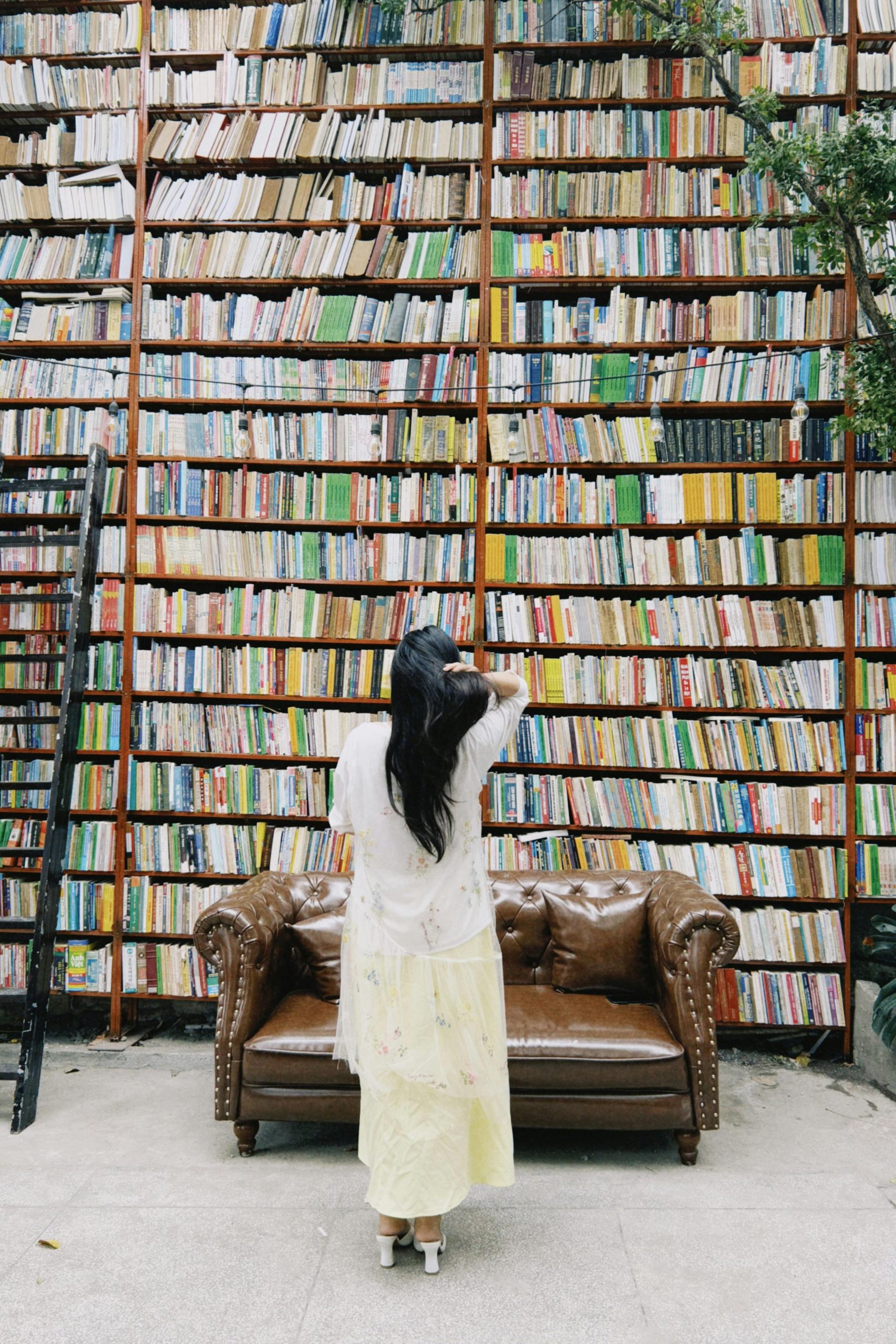 A woman facing a massive bookshelf in a library, contemplating her next read.
