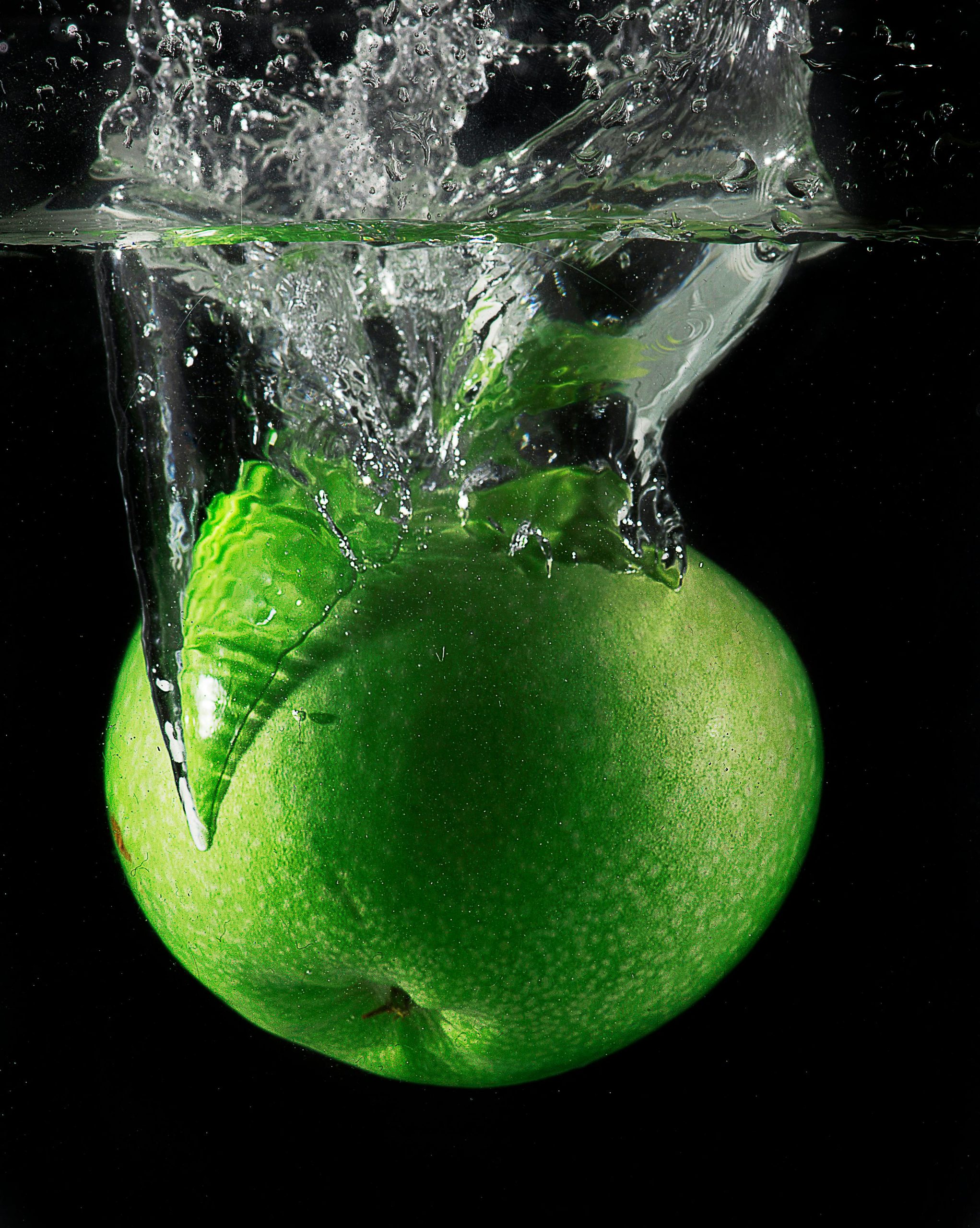 Crisp green apple diving into water with a splash against a black background.